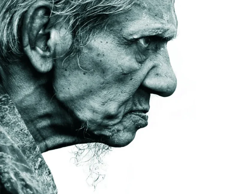 Perfil en primer plano de una persona mayor con barba larga, rostro arrugado y fondo blanco, en tonos azul verdoso monocromáticos.