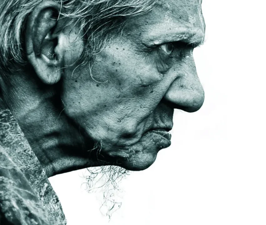 Perfil en primer plano de una persona mayor con barba larga, rostro arrugado y fondo blanco, en tonos azul verdoso monocromáticos.