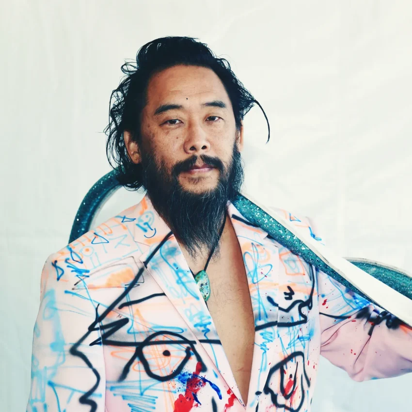 Persona con chaqueta estilo graffiti, collar turquesa y accesorio brillante en forma de serpiente sobre los hombros, en fondo blanco. Obra de David Choe.