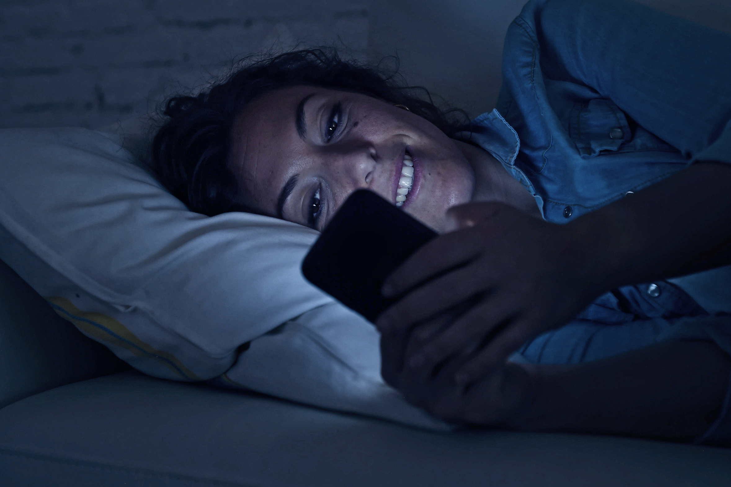 young beautiful woman lying on home couch using mobile phone tex