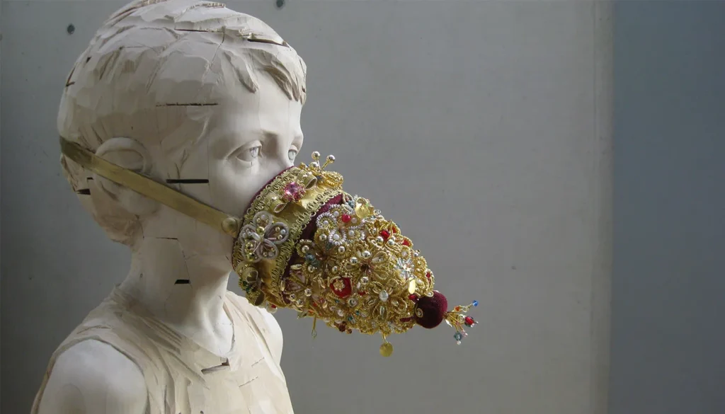 Escultura de madera de una niña con un elaborado bozal dorado decorado con perlas y abalorios, obra contemporánea de Gehard Demetz.