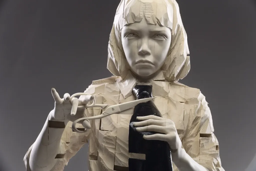 Escultura de figura humana con expresión solemne, sosteniendo tijeras y botella negra; combinación de madera tallada y material blanco pulido.