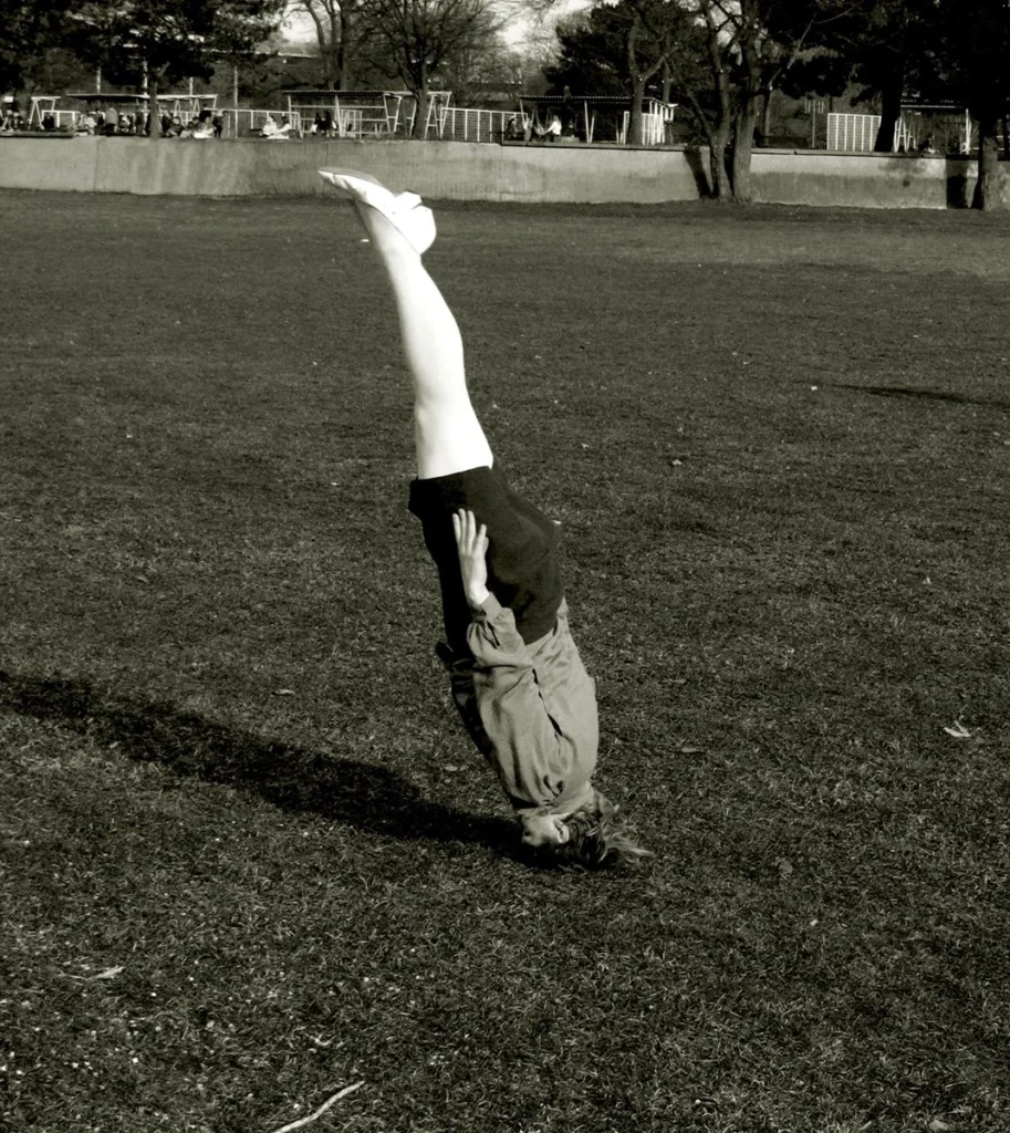 “Figura femenina en equilibrio invertido sobre césped, fotografía conceptual de Isabelle Wenzel.”