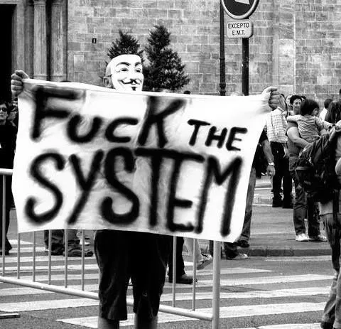Persona con máscara de Guy Fawkes sosteniendo pancarta en protesta