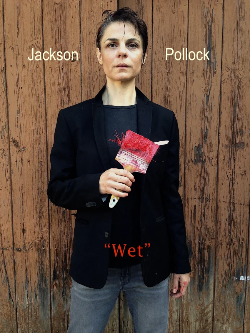 Concha Vidal sosteniendo un gran pincel rojo en la performance “WET”, evocando la energía gestual de Jackson Pollock.