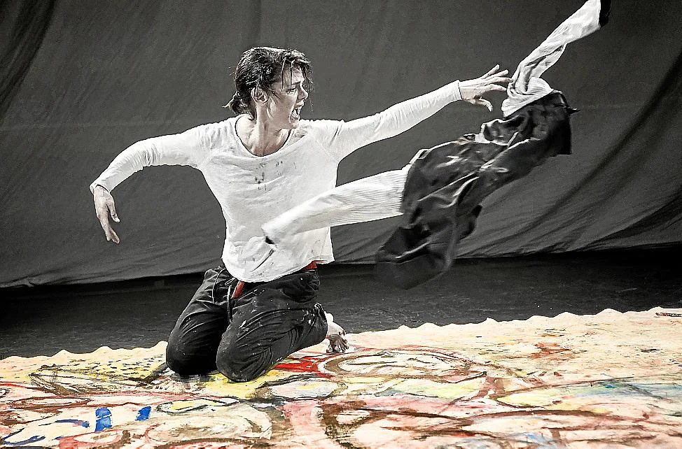 Concha Vidal arrodillada en plena acción performativa durante “WET”, con una prenda en vuelo sobre el lienzo pintado.