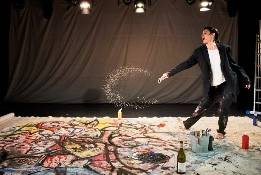 Concha Vidal pintando descalza sobre un gran lienzo durante la performance “WET”, con una salpicadura de color en pleno aire.