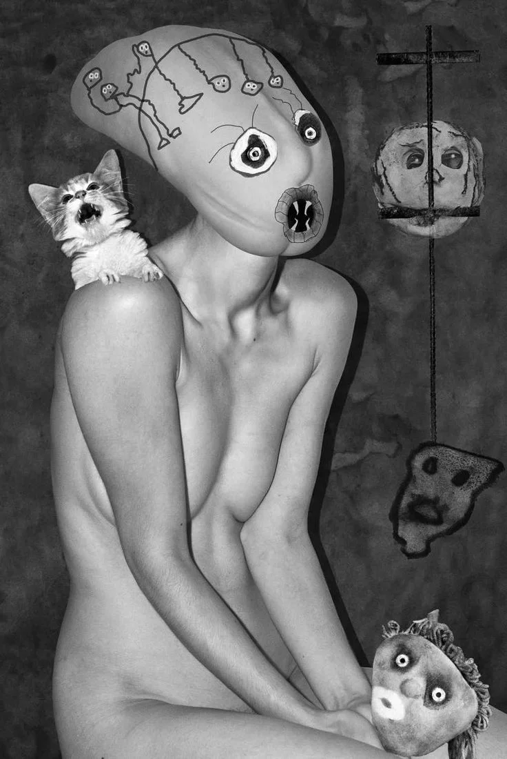 Figura desnuda con máscara surreal y gato sobre el hombro, rodeada de rostros suspendidos en blanco y negro.