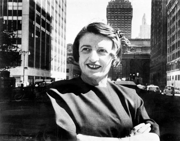 Retrato en blanco y negro de Ayn Rand en Manhattan, con expresión confiada y fondo arquitectónico emblemático.