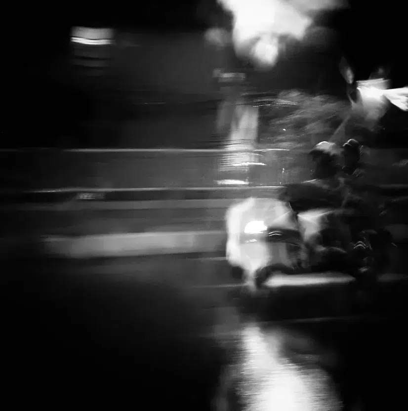 Silueta de motociclista en calle mojada con reflejos urbanos
