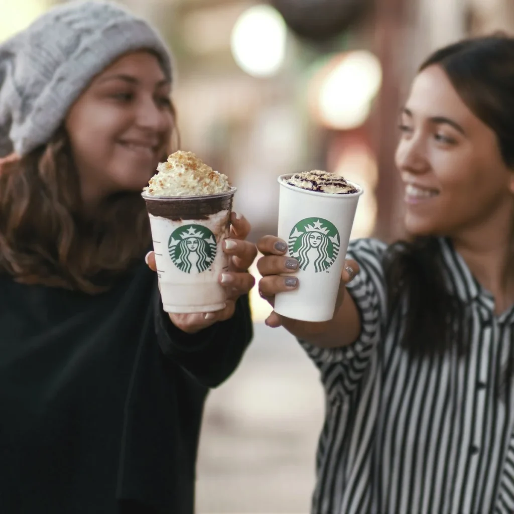 Personas brindando con bebidas de Starbucks mientras sonríen en un ambiente urbano.