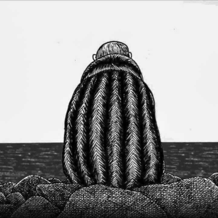 Persona con capa tejida sentada en la costa rocosa, mirando al océano.