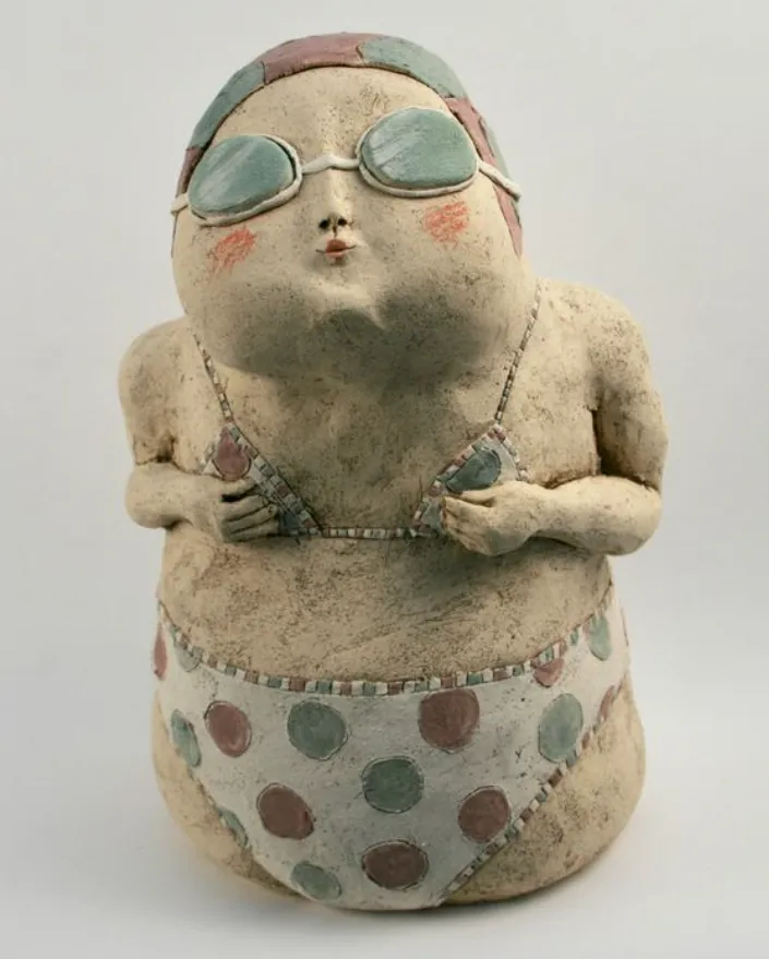 Escultura de Anne-Sophie Gilloen de cerámica de una bañista con bikini de lunares, gorro de baño y gafas, en pose divertida y estilizada.