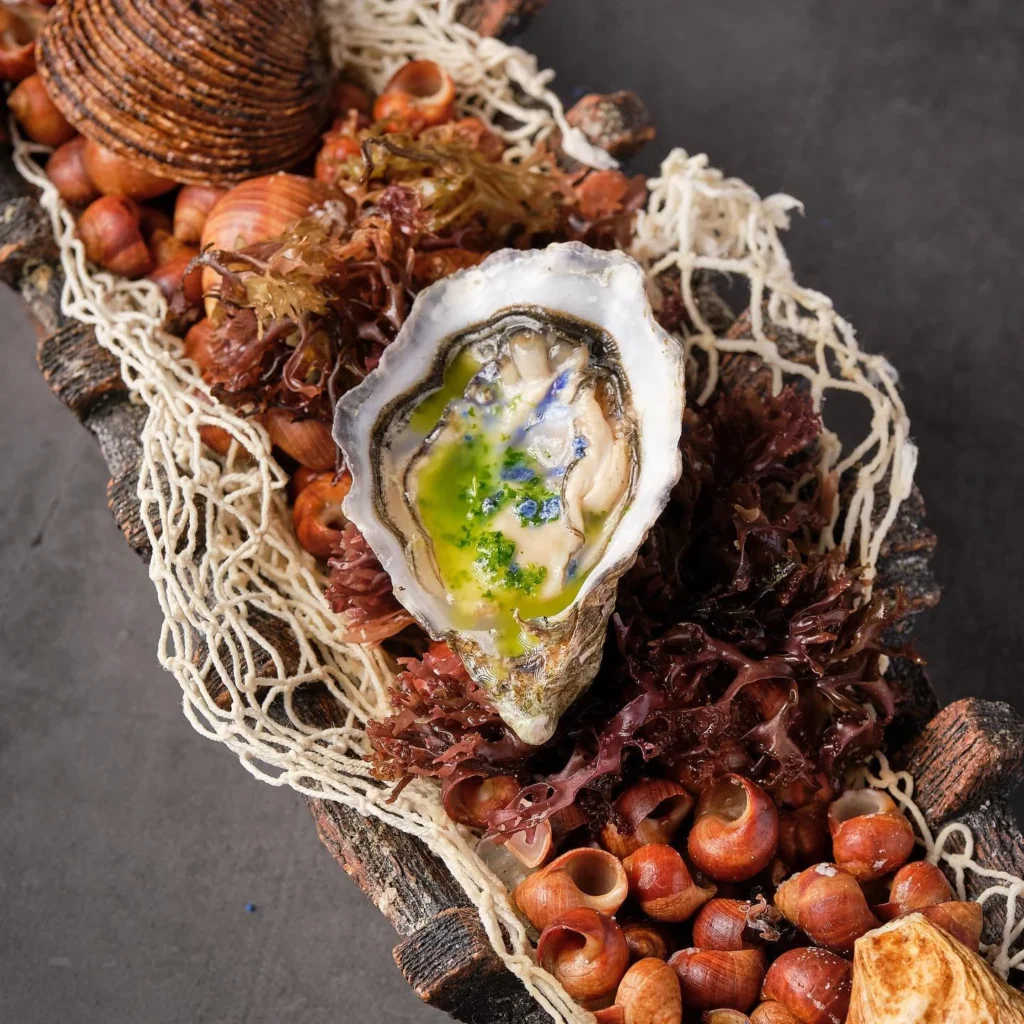 Ostra fresca con salsa verde y flores comestibles presentada sobre madera con algas y mariscos en La Vieja de Jonay Palma de Mallorc