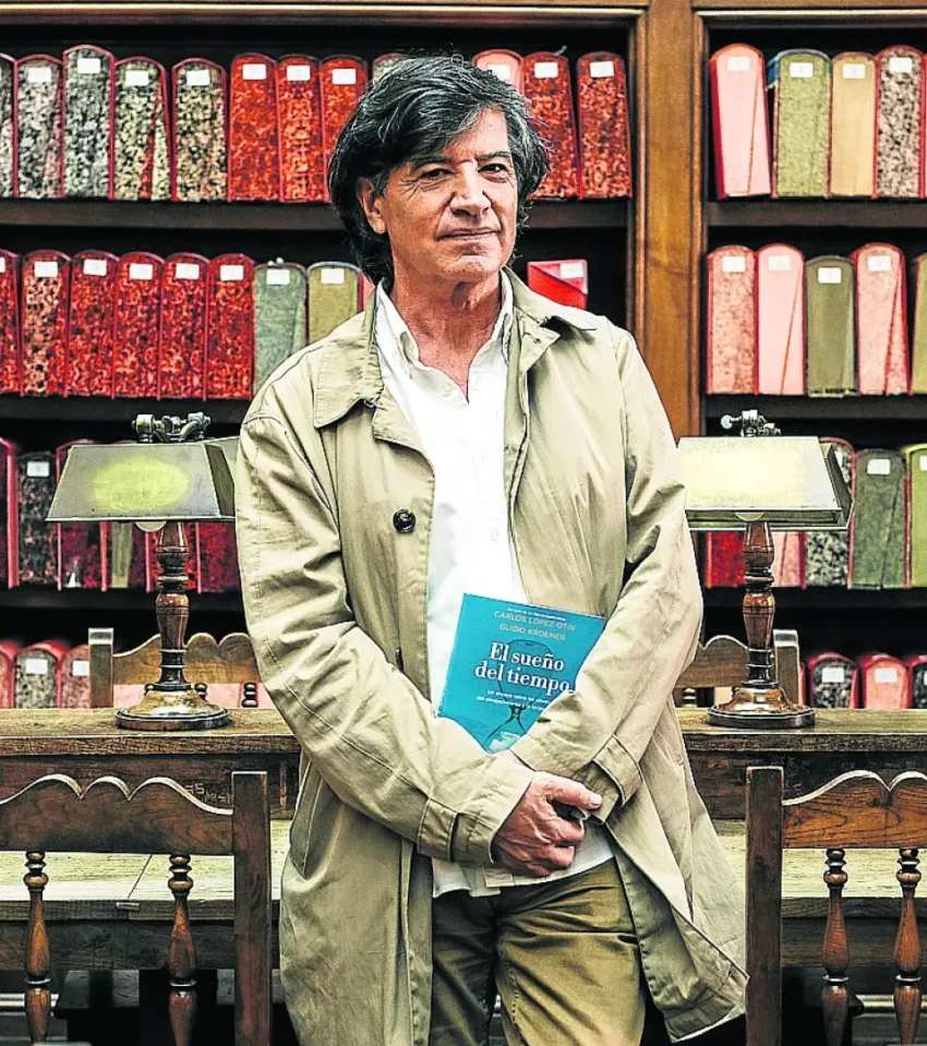 Carlos González Reigosa sostiene su libro “El sueño del tiempo” en una sala de archivo con estanterías coloridas.