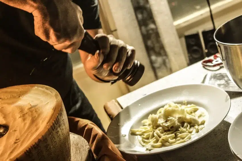 Plato de pasta recién servido, sazonado con pimienta negra y queso parmesano extraído directamente de una rueda.