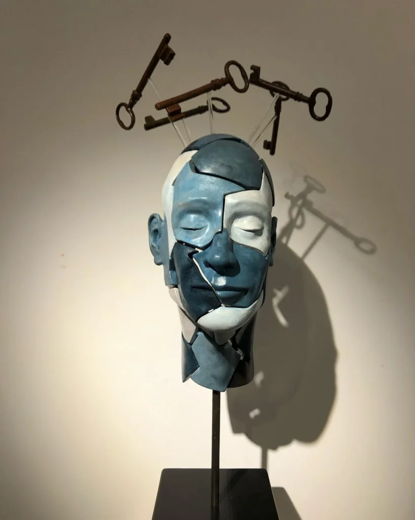 Escultura conceptual de Miguel Monegal: cabeza segmentada con llaves suspendidas sobre fondo neutro.