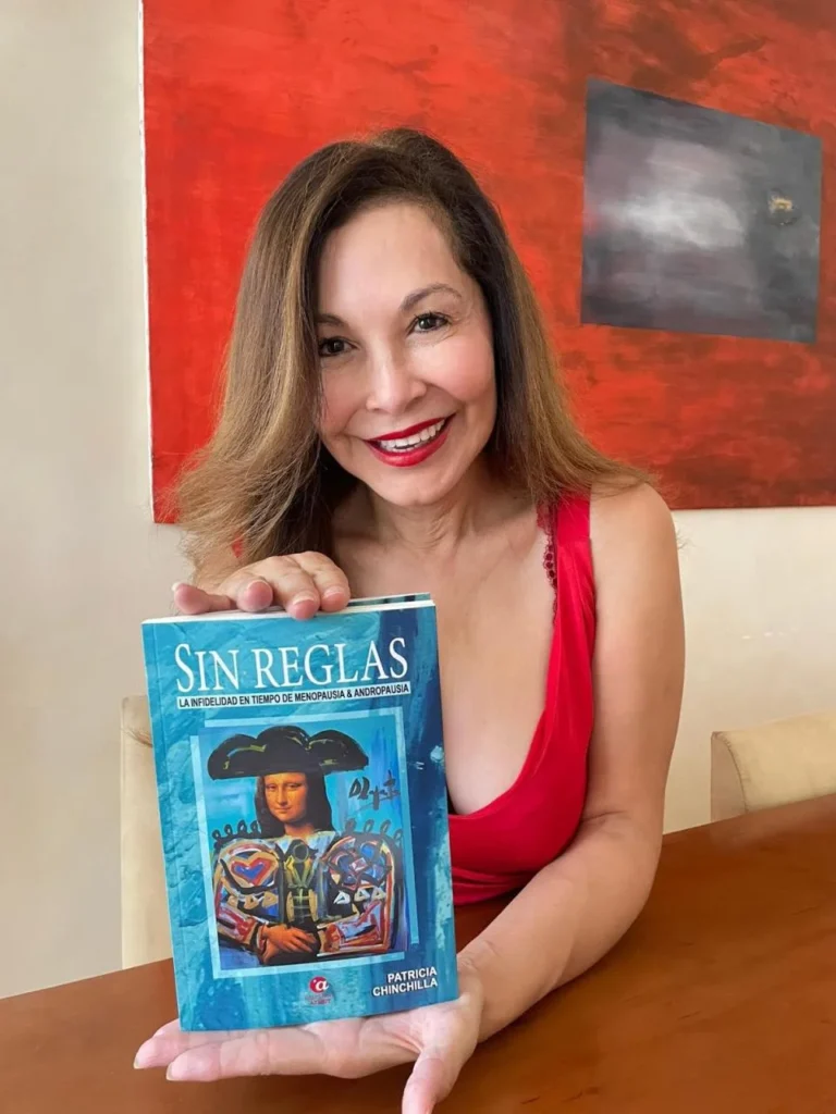 Patricia Chinchilla sostiene su libro “Sin reglas” en una mesa de madera, con fondo de pintura abstracta.