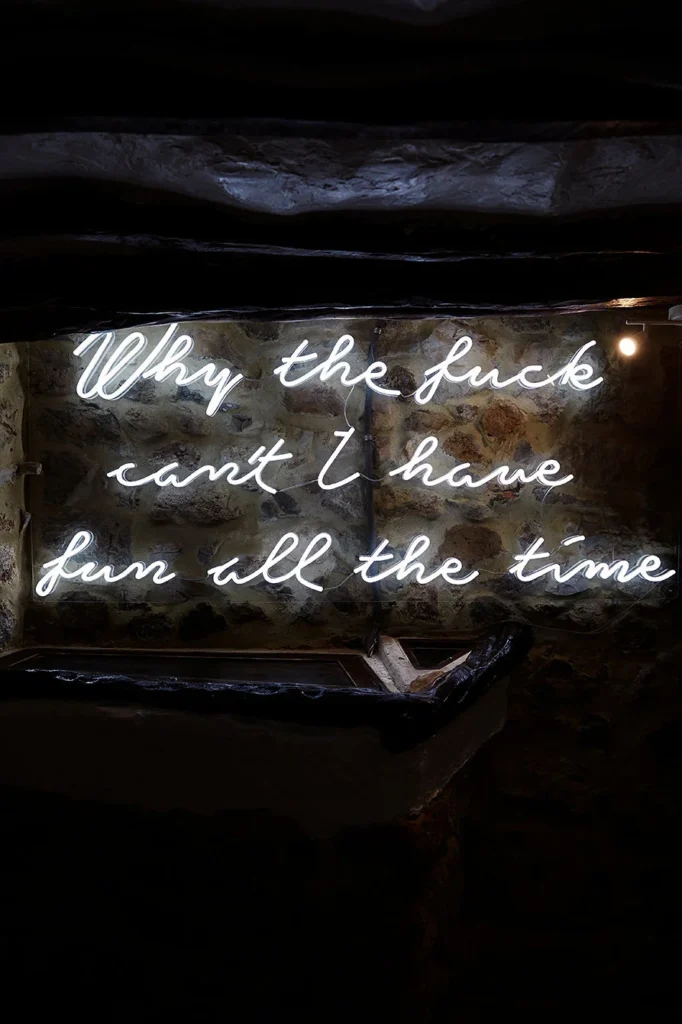 Neón con frase irreverente sobre muro de piedra en Pikes Ibiza.