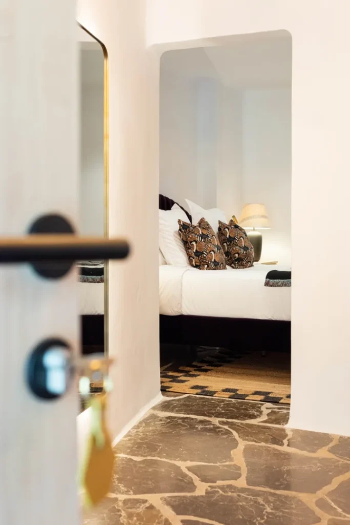 Habitación de Pikes Ibiza vista desde una puerta entreabierta, con cama blanca y luz cálida.