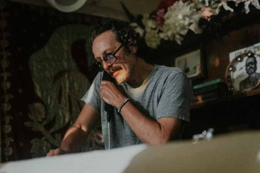 DJ Harvey hablando al micrófono en un ambiente íntimo con iluminación cálida y decoración artística.