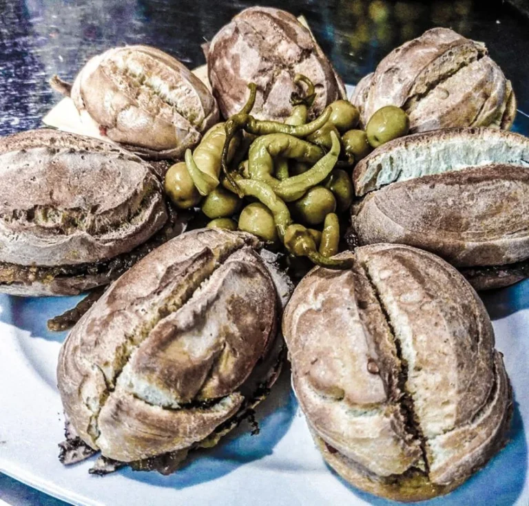 Plato con varios llonguets rellenos acompañados de aceitunas y guindillas verdes.