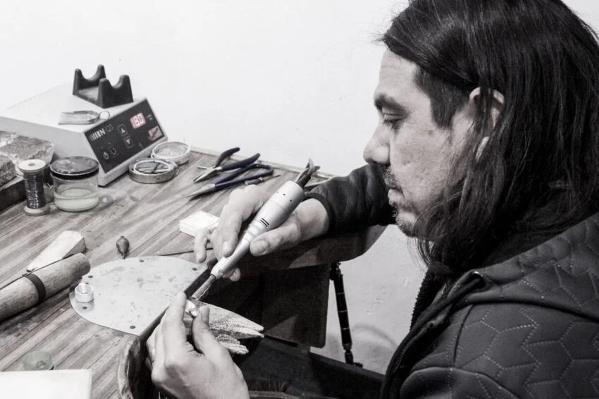 Artesano trabajando una pieza de joyería en su banco de trabajo con herramientas manuales.