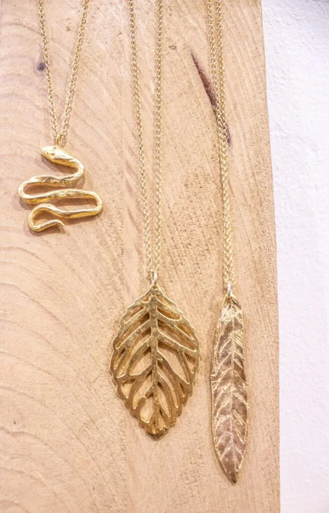 Collares artesanales con colgantes dorados inspirados en una serpiente, una hoja y una pluma.