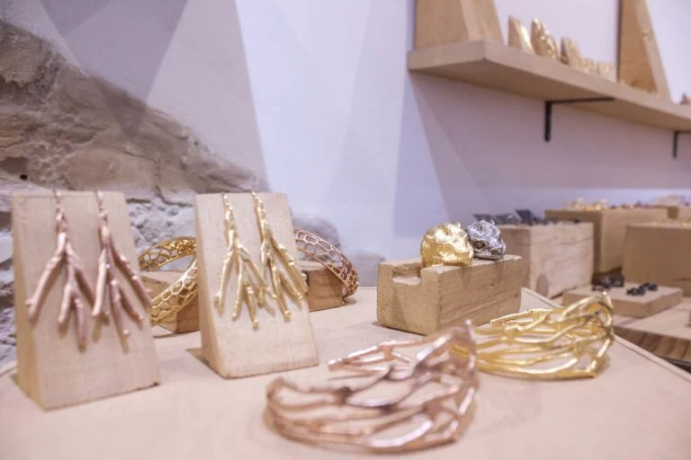 Exposición de pendientes, anillos y pulseras artesanales en tonos dorados sobre soportes de madera.