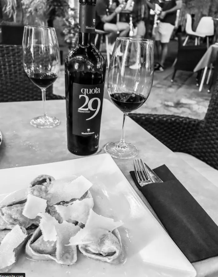 Botella de vino Quota 29 con dos copas y plato de ravioli con parmesano en mesa de restaurante.