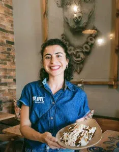 Ceci Velázquez sonriente con camisa de Xólotl sosteniendo un postre decorado con nata y chocolate