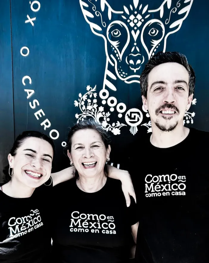 “Como en México como en casa” frente a mural azul con ilustración de animal estilizado