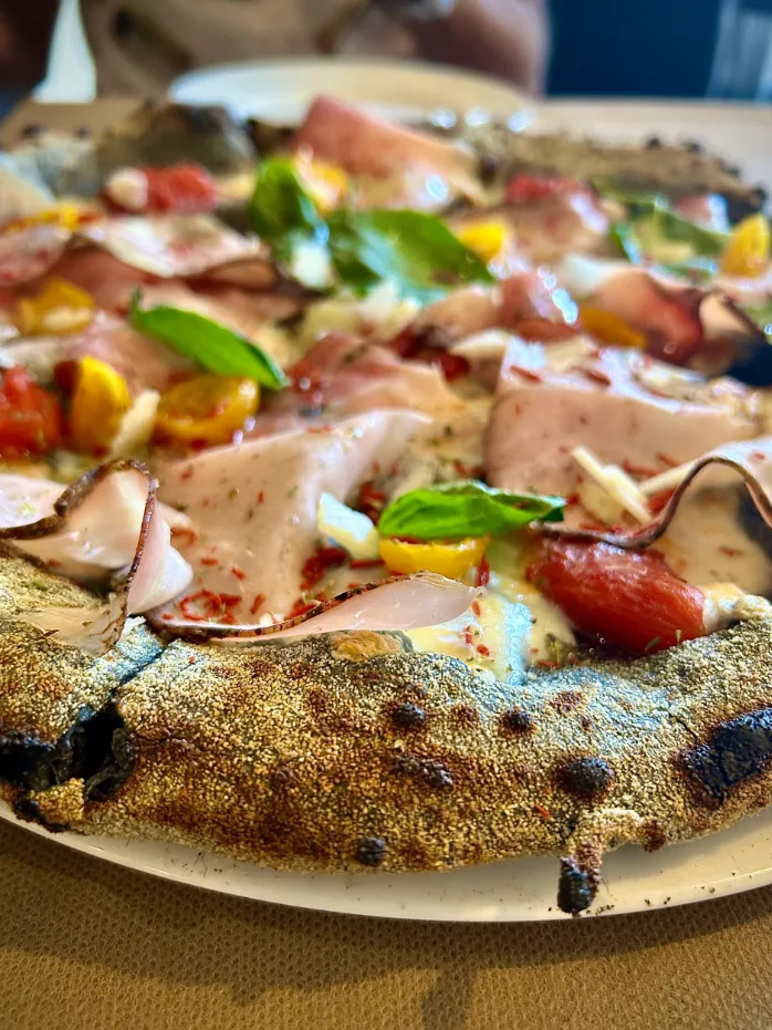 Pizza gourmet con mortadela, albahaca fresca, tomates cherry y borde rústico sobre plato blanco.