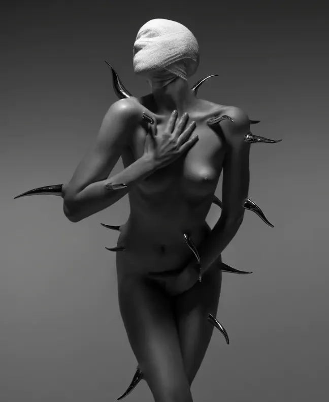 Figura humana desnuda con la cabeza vendada y protuberancias metálicas, en pose introspectiva sobre fondo gris degradado.