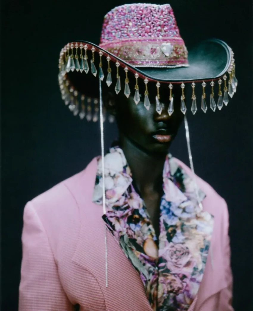 Persona con sombrero cowboy rosa adornado con cristales, blazer rosa y camisa floral; estilo visual audaz y ornamental.