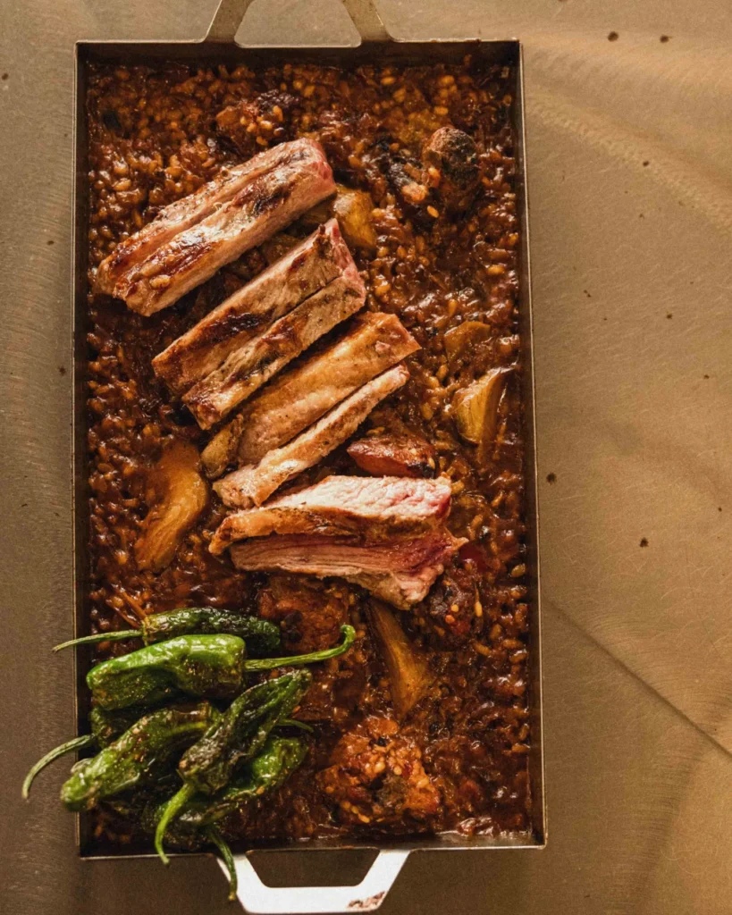 Arroz a la llauna, ese recipiente ancestral que concentra sabores y memorias, reposa un arroz que parece respirar el aire salino del litoral.