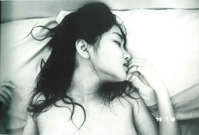 Fotografía en blanco y negro de Nobuyoshi Araki que muestra a una figura femenina recostada, con gesto sereno y atmósfera íntima que evoca deseo, duelo y contemplación.