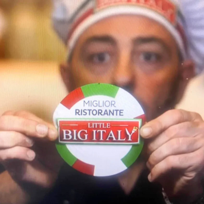 Dario Zappala con gorro de chef sosteniendo un cartel con los colores de la bandera italiana y el texto “Miglior Ristorante – Little Big Italy”
