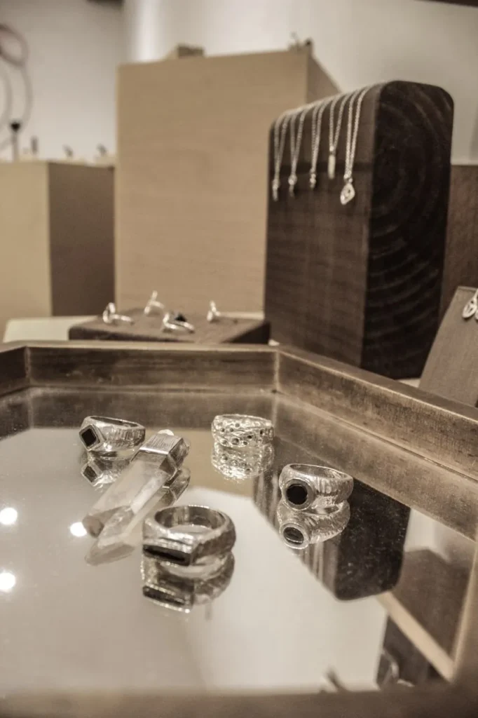 Anillos y colgantes artesanales sobre bandeja de espejo y soportes de madera – Rako Joies