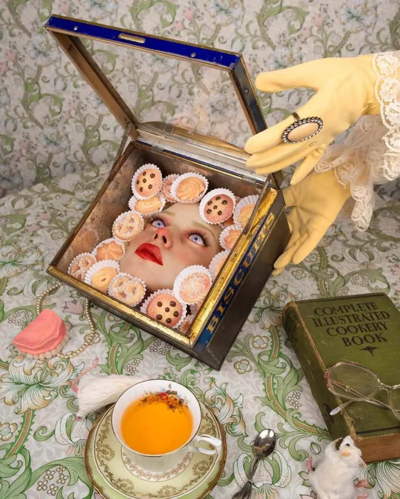 Caja vintage de galletas abierta revela un rostro humano entre cupcakes, con mano enguantada levantando la tapa; fondo floral y libro de cocina antiguo completan la escena surrealista.