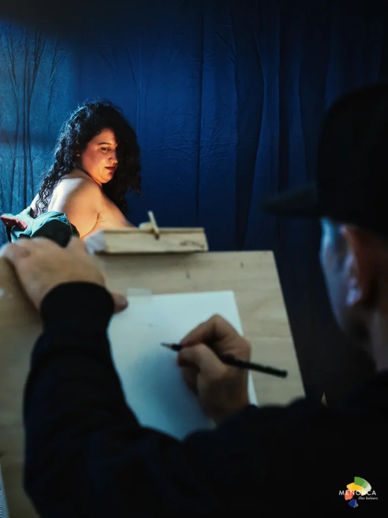 Artista dibujando a un modelo iluminado por luz cálida durante una sesión de estudio del cuerpo en Quarantine 2025.