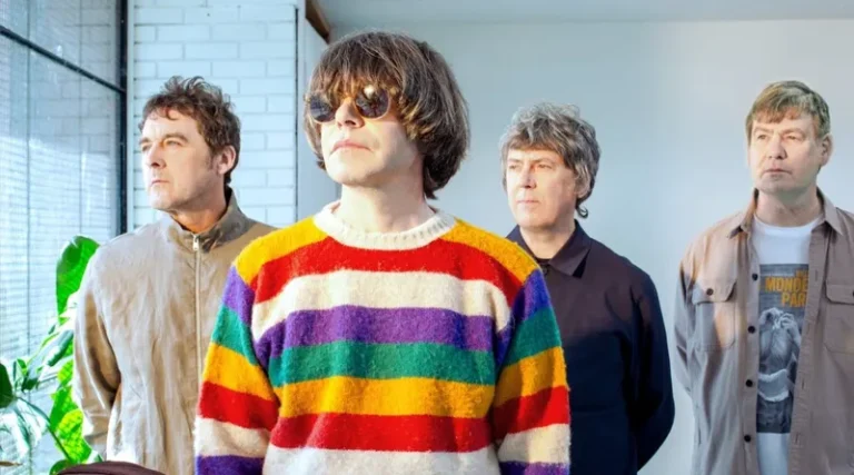 Miembros de The Charlatans posando en interior con luz natural, destacando el estilo colorido y contrastado del vocalista.