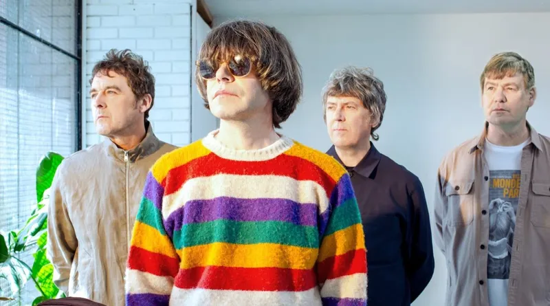 Miembros de The Charlatans posando en interior con luz natural, destacando el estilo colorido y contrastado del vocalista.