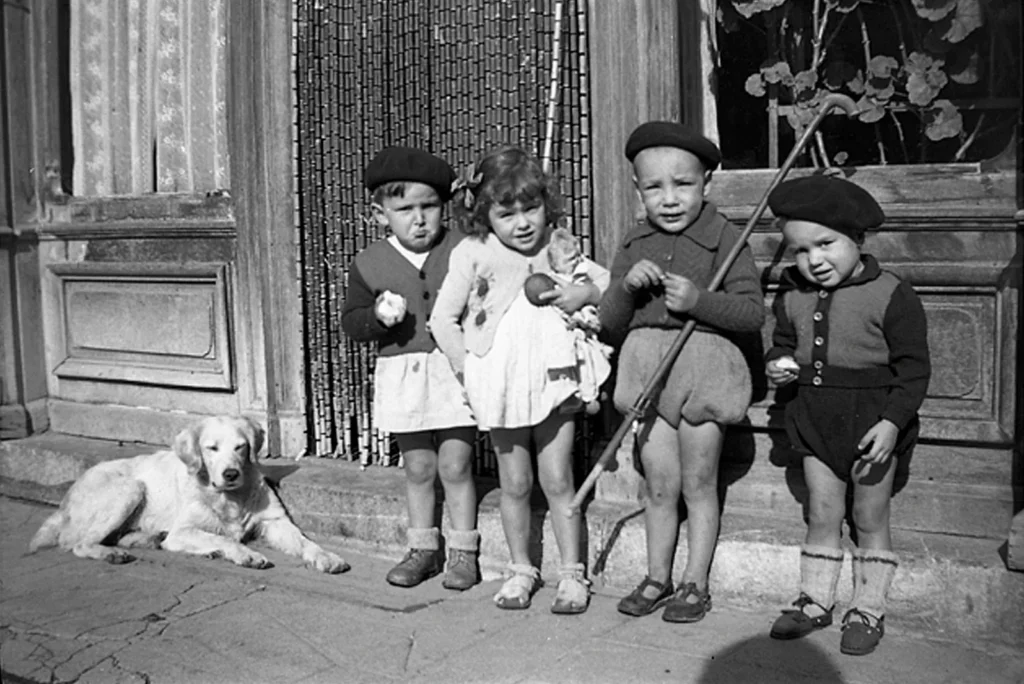 Fotografía de Vivian Maier: cuatro niños frente a una puerta con cortina de cuentas y un perro acostado