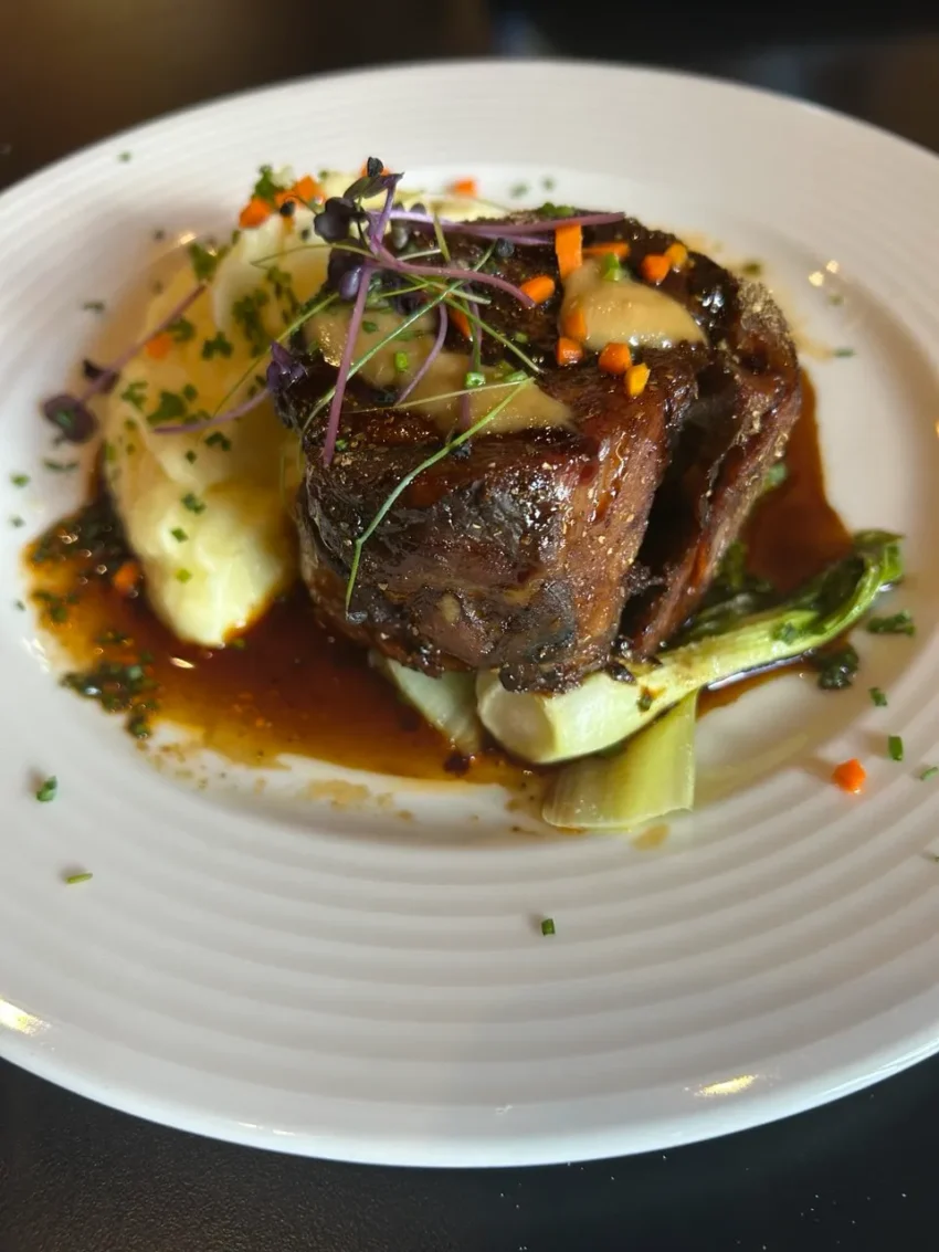 Paletilla de cordero deshuesada rellena de sobrasadoa, con puré de patatas y pak choi, presentada con salsa reducida y microgreens.