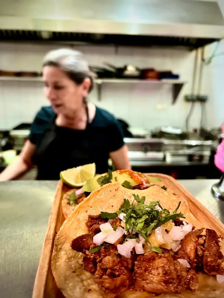 Tacos de carne asada con cilantro y cebolla sobre bandeja de madera en cocina mexicana