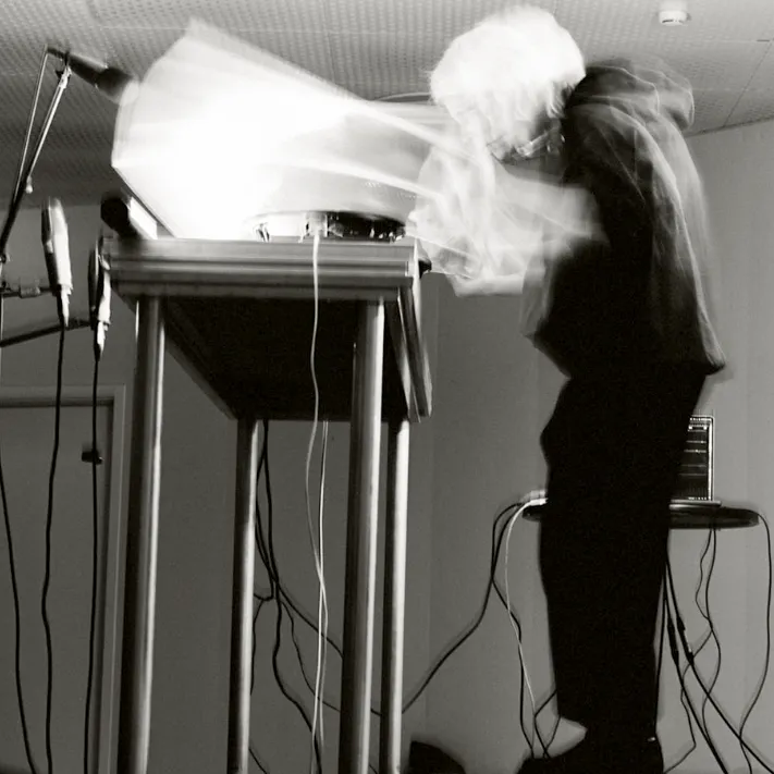 Ash Fure manipulando dispositivos sonoros durante una performance en vivo, rodeada de micrófonos y cables, en un entorno técnico y vibrante.