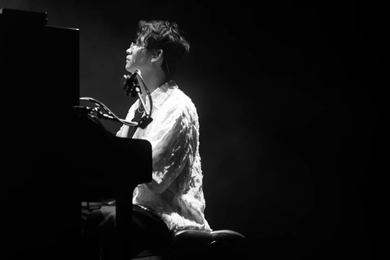 Pianista tocando en un concierto en ambiente oscuro, iluminado lateralmente mientras interpreta una pieza en el Jazz Voyeur Festival.