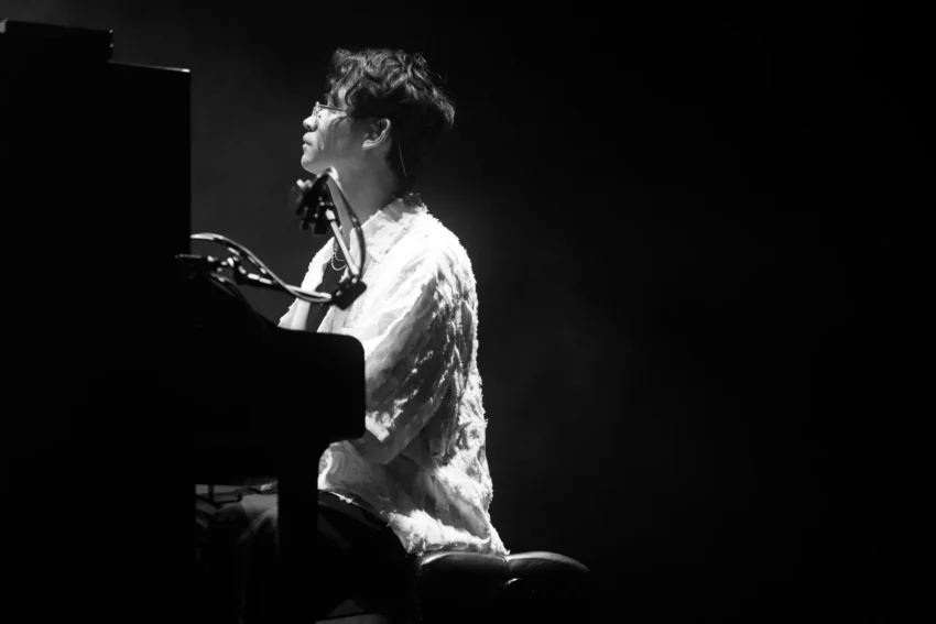 Pianista tocando en un concierto en ambiente oscuro, iluminado lateralmente mientras interpreta una pieza en el Jazz Voyeur Festival.