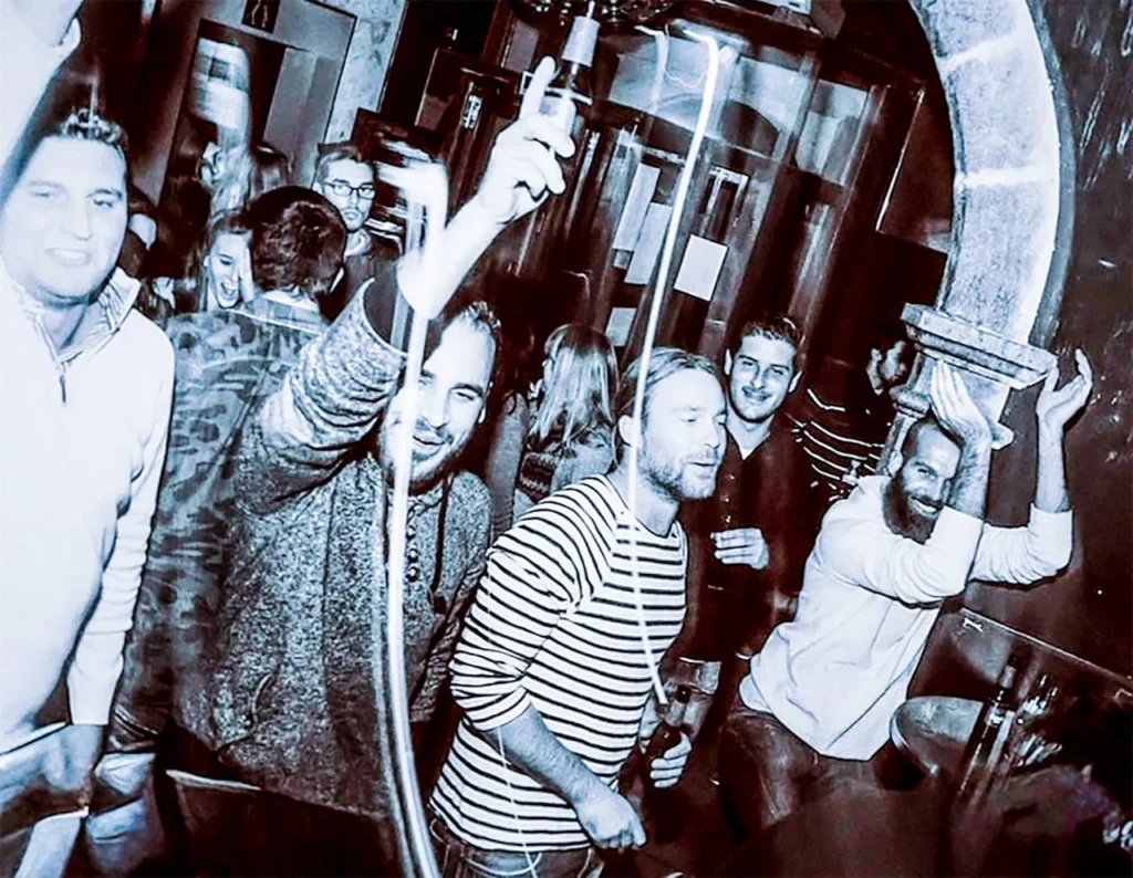 Grupo de personas celebrando con vino en el interior de Acros Café Bar de Alaró, bajo iluminación festiv